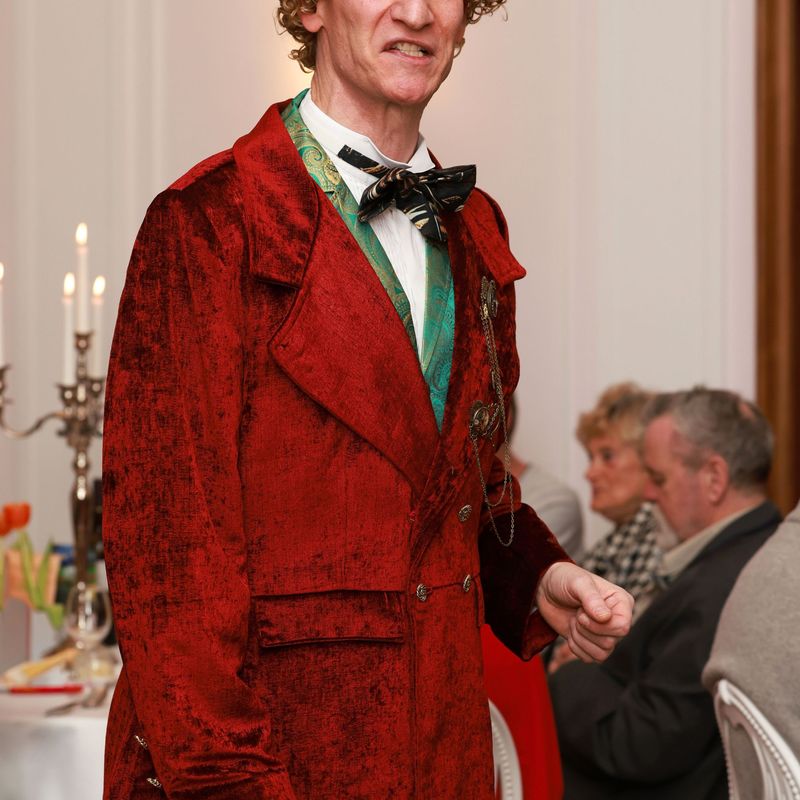 Ganzkörperbild von Sir John mit Locken und rotem Gehrock und Gehstock