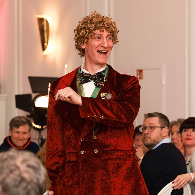 Sir John im roten Gehrock fröhlich mit Gästen