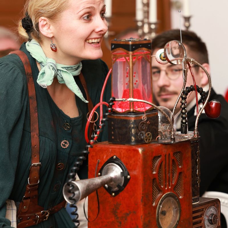 Phoebe mit Maschine und einem Gast im historischen Kostüm 