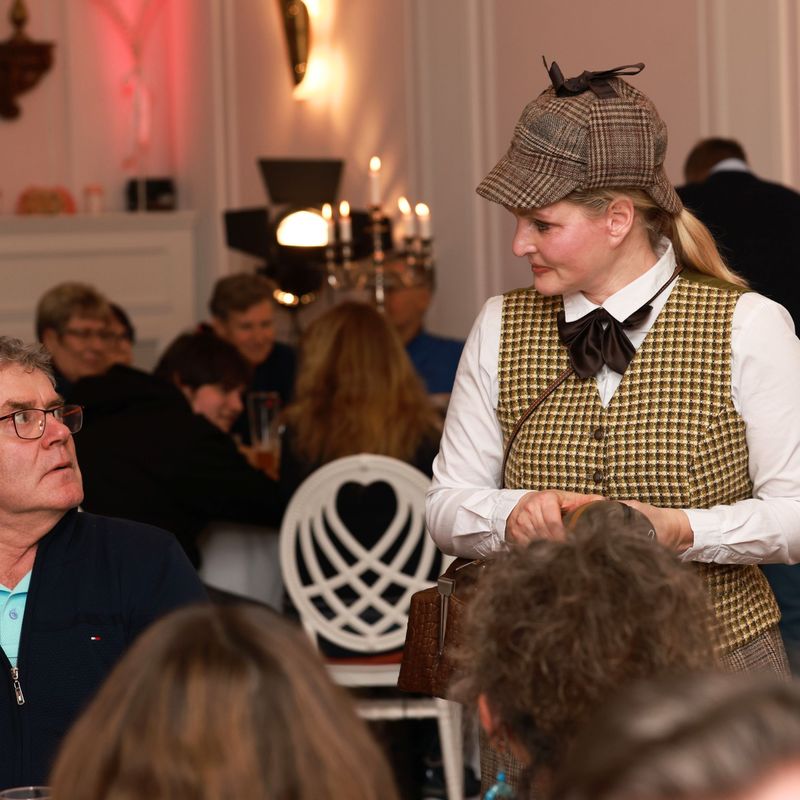 Eliza im Sherlock Look spricht mt einem Gast am Tisch