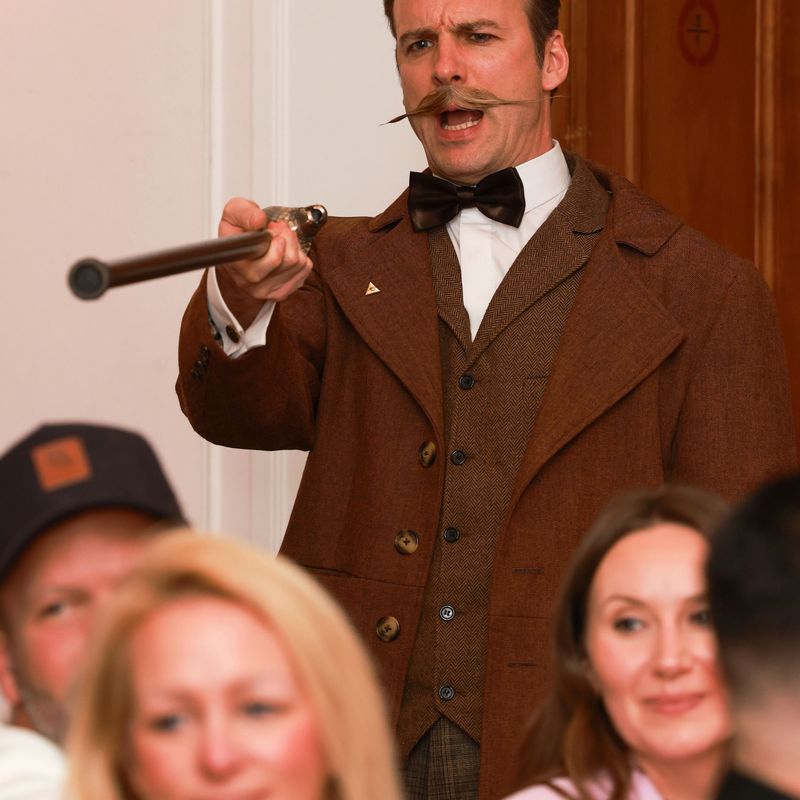 Conan Doyle mit Gästen deutet energisch mit Gehstock