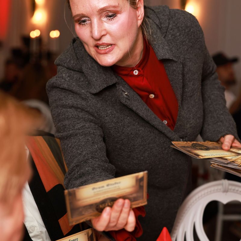 Frau verteilt Tischkarten an Gäste beim Dinnertheater